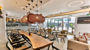 A modern dining area with a long wooden table and multiple chairs, surrounded by large windows offering views of the city. - Hotel Plaza (Budva)