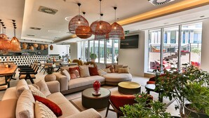 A modern hotel lobby with a large seating area, a bar, and large windows offering a view of the outside. - Hotel Plaza (Budva)