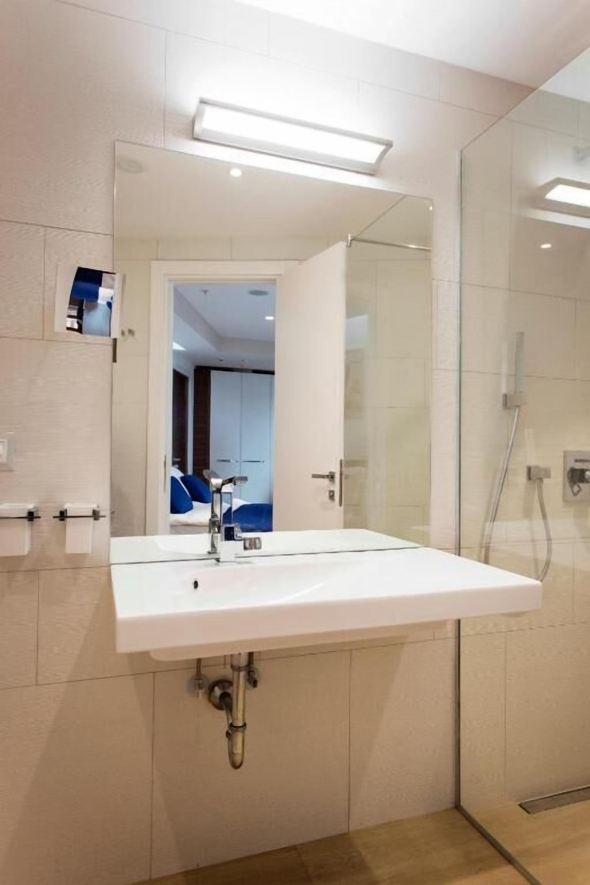 Ein modernes Badezimmer mit großem Spiegel, weißem Waschbecken und einer Duschkabine aus Glas.