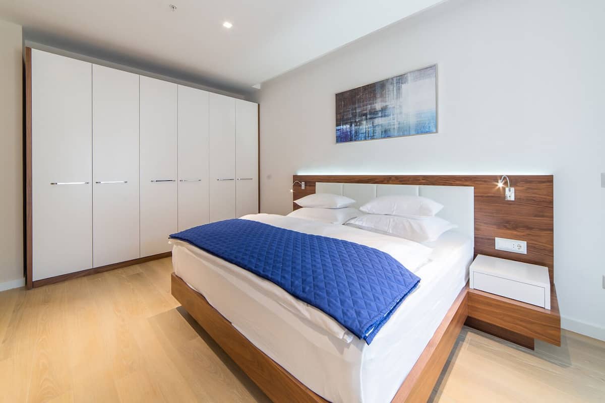 A modern bedroom with a large bed, a wardrobe, a nightstand, and a painting on the wall.