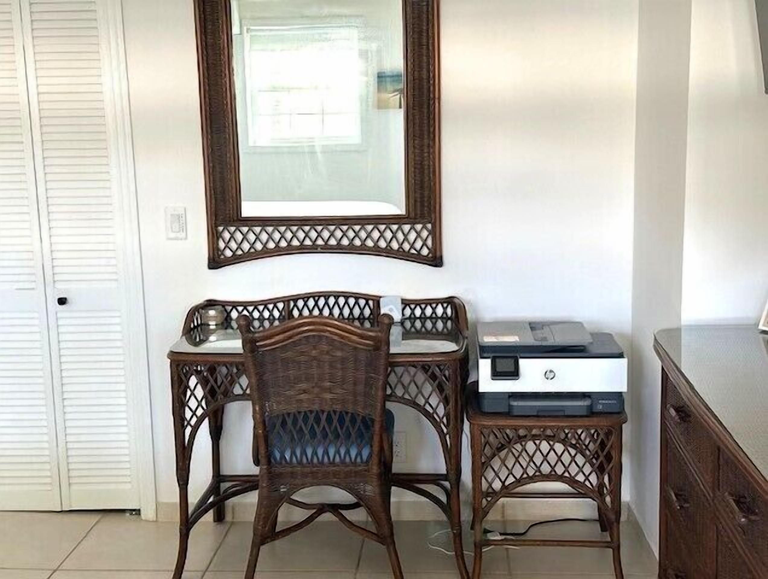 A room with a desk, chair, printer, and a large mirror on the wall.