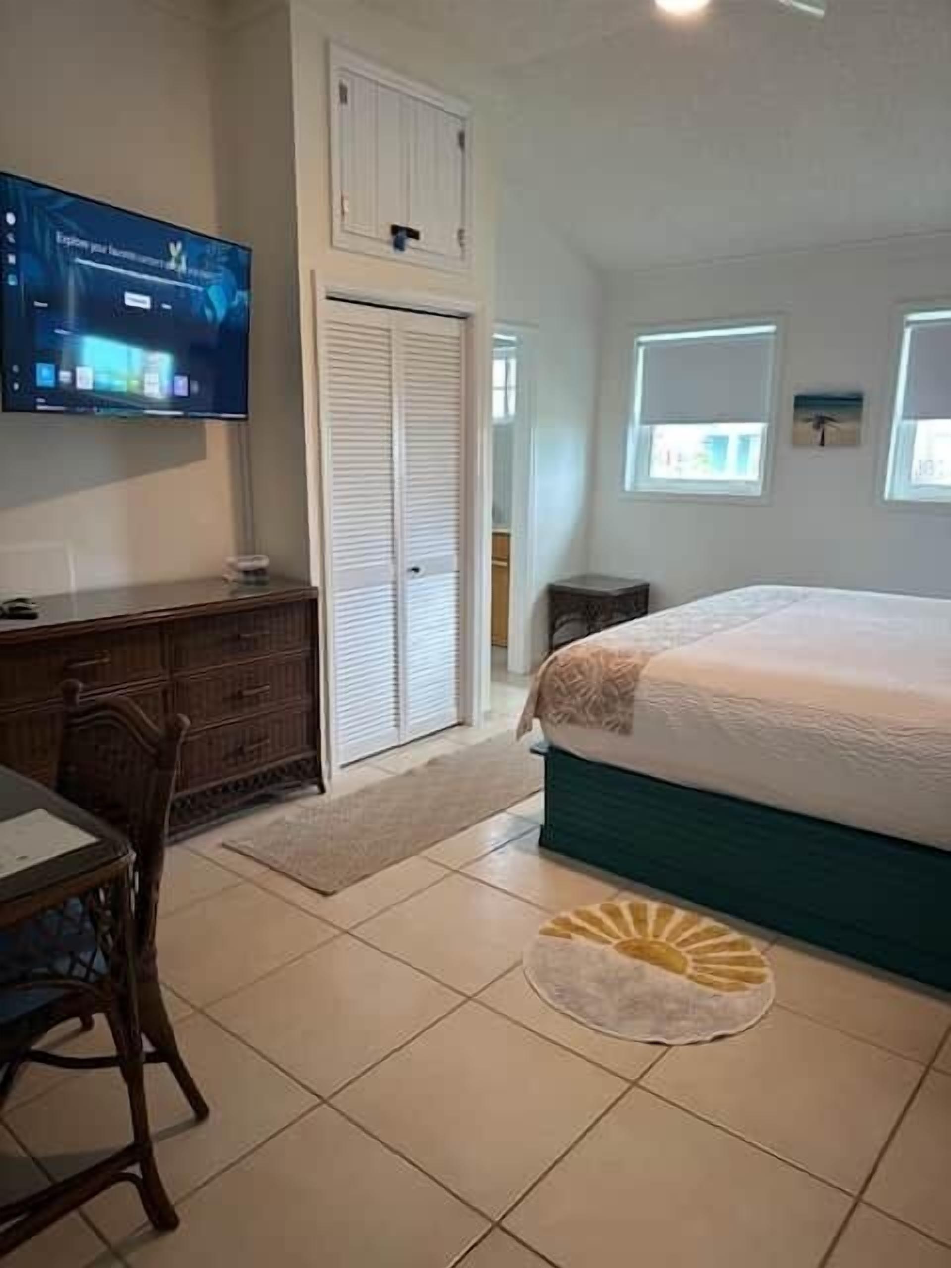 A bedroom with a bed, a TV mounted on the wall, a desk, and a wardrobe.