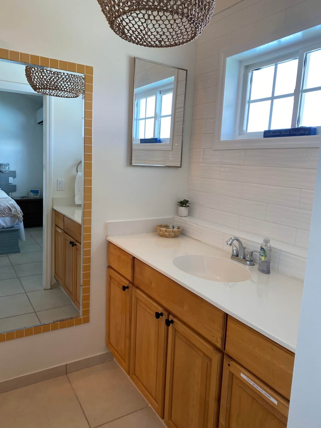 A bathroom with a large mirror, wooden cabinets, a white sink, and a window above the sink.