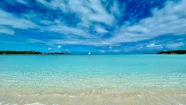 A beach with clear turquoise water, a sandy shore, and a distant boat. - Exuma Oceanfront-Steps to the beach-Side Quest (George Town Exuma)