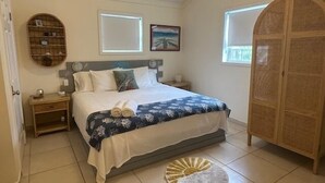 A bedroom with a bed, bedside tables, a wardrobe, a round rug, and a window. - Exuma Oceanfront-Steps to the beach-Side Quest (George Town Exuma)