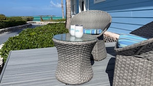 A wicker table with two white mugs, a striped cushion, and a view of the ocean. - Exuma Oceanfront-Steps to the beach-Side Quest (George Town Exuma)