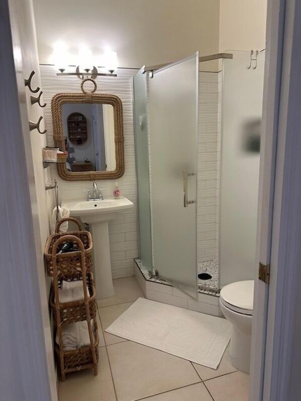 A bathroom with a glass shower enclosure, a sink with a mirror, and a wicker basket.