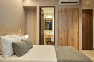 Habitación de hotel con cama, un armario de madera, baño visible a través de una puerta abierta y aire acondicionado instalado en el techo.