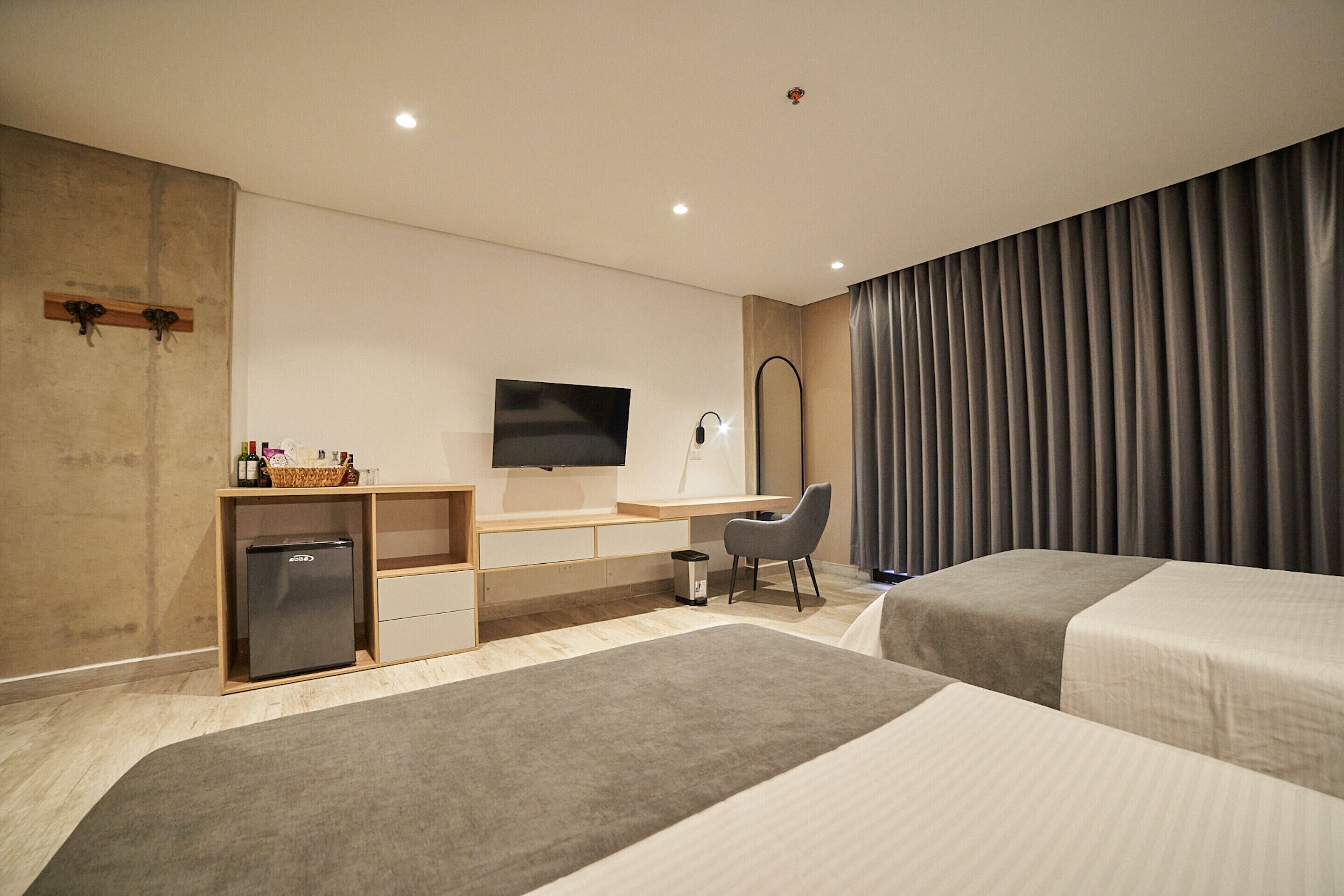 A hotel room with two beds, a desk with a computer, a TV, and a minibar.