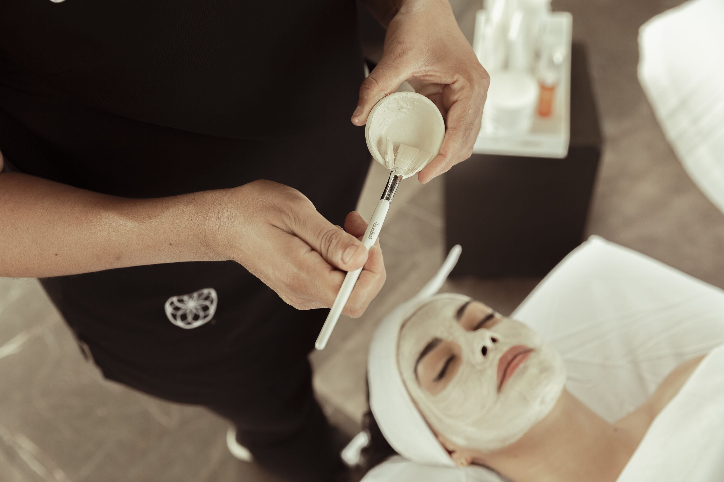 A person applying a facial mask to a client.