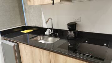 Una cuina moderna amb taulell negre, rentamics d'acer inoxidable i una cafetera.