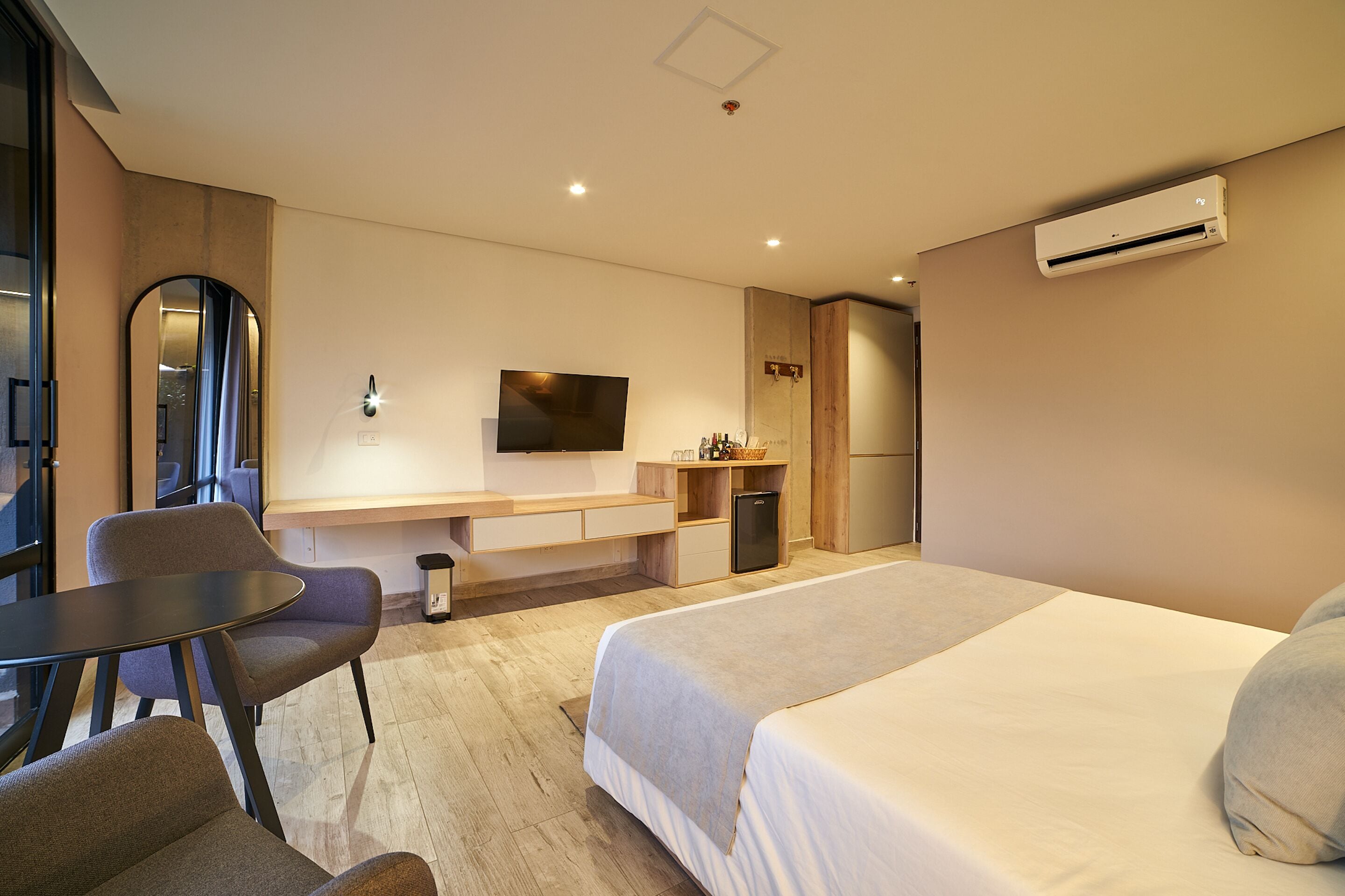 Una habitación de hotel moderna con cama, escritorio, silla, televisor y aire acondicionado.