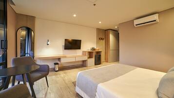 Una habitación de hotel moderna con cama, escritorio, silla, televisor y aire acondicionado.
