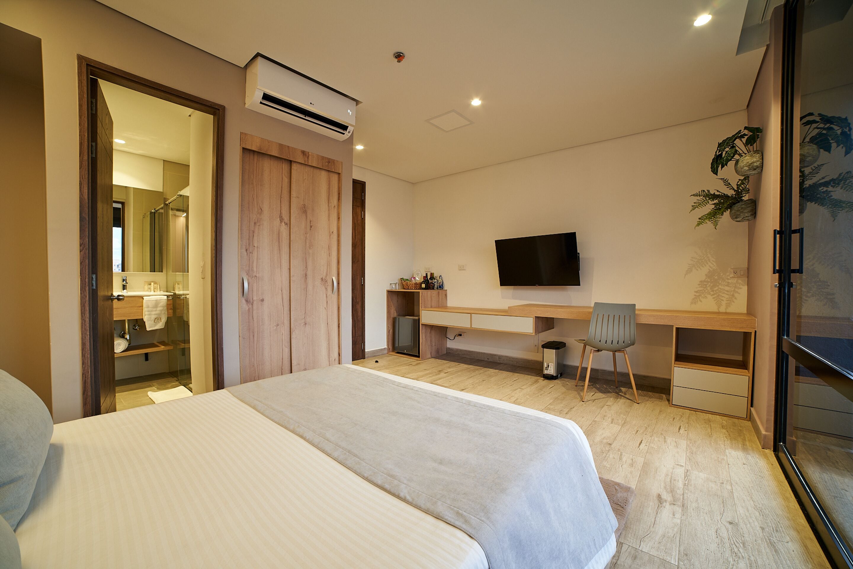 A bedroom with a bed, a desk, a chair, a TV, and an air conditioning unit.