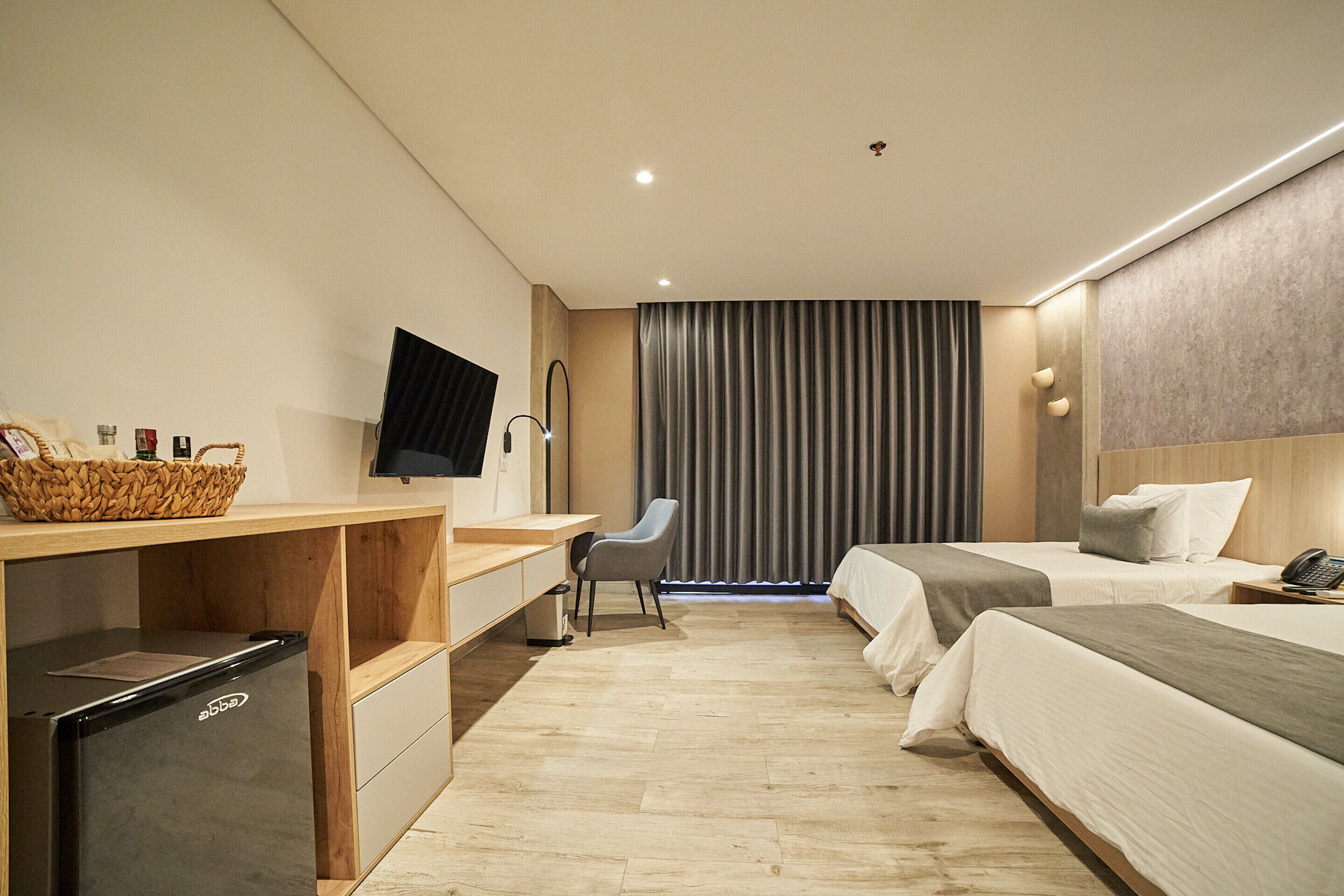 A hotel room with a desk, chair, two beds, a television, and a small refrigerator.