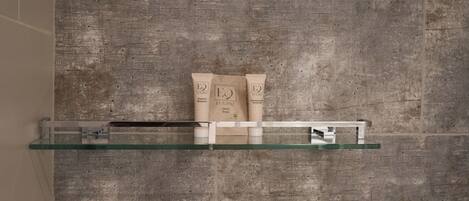 A bathroom with a glass shelf holding toiletries against a textured wall.