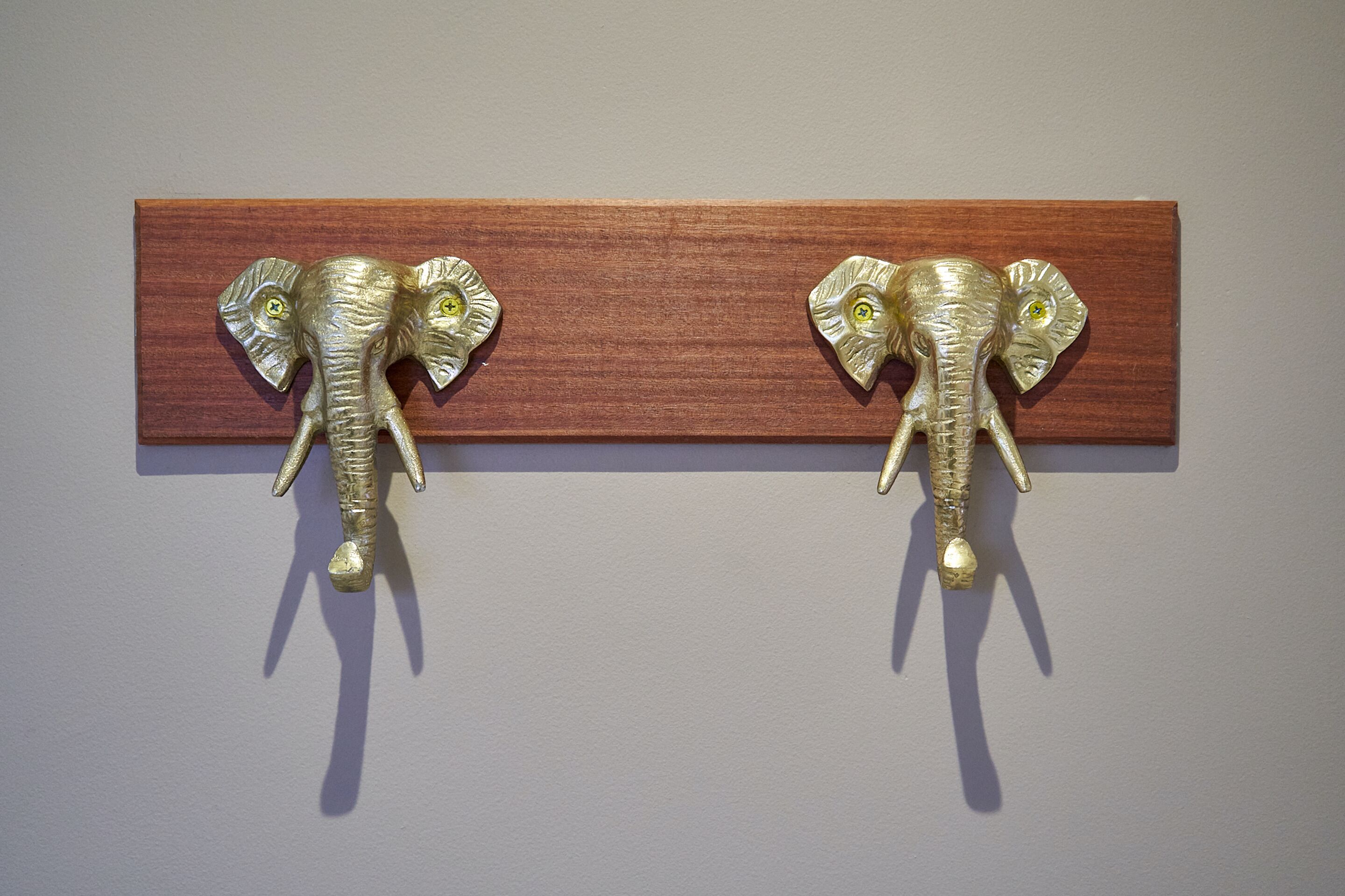Deux crochets muraux en métal, en forme d’éléphant, fixés sur un panneau en bois.