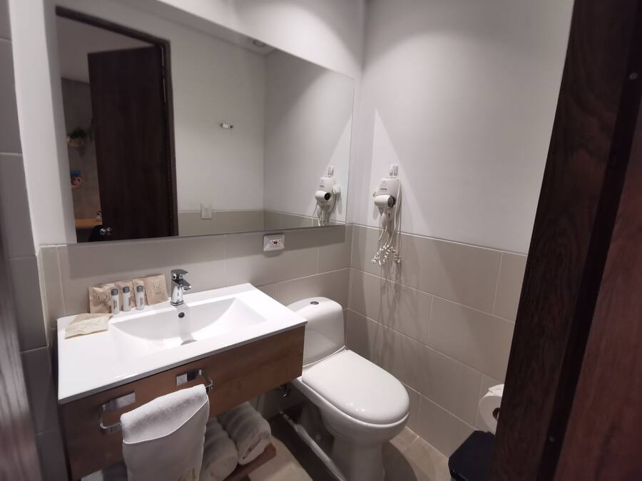 A modern bathroom with a white sink, vanity, and toilet. There is a towel rack with towels, a mirror above the sink, and a hairdryer mounted on the wall.