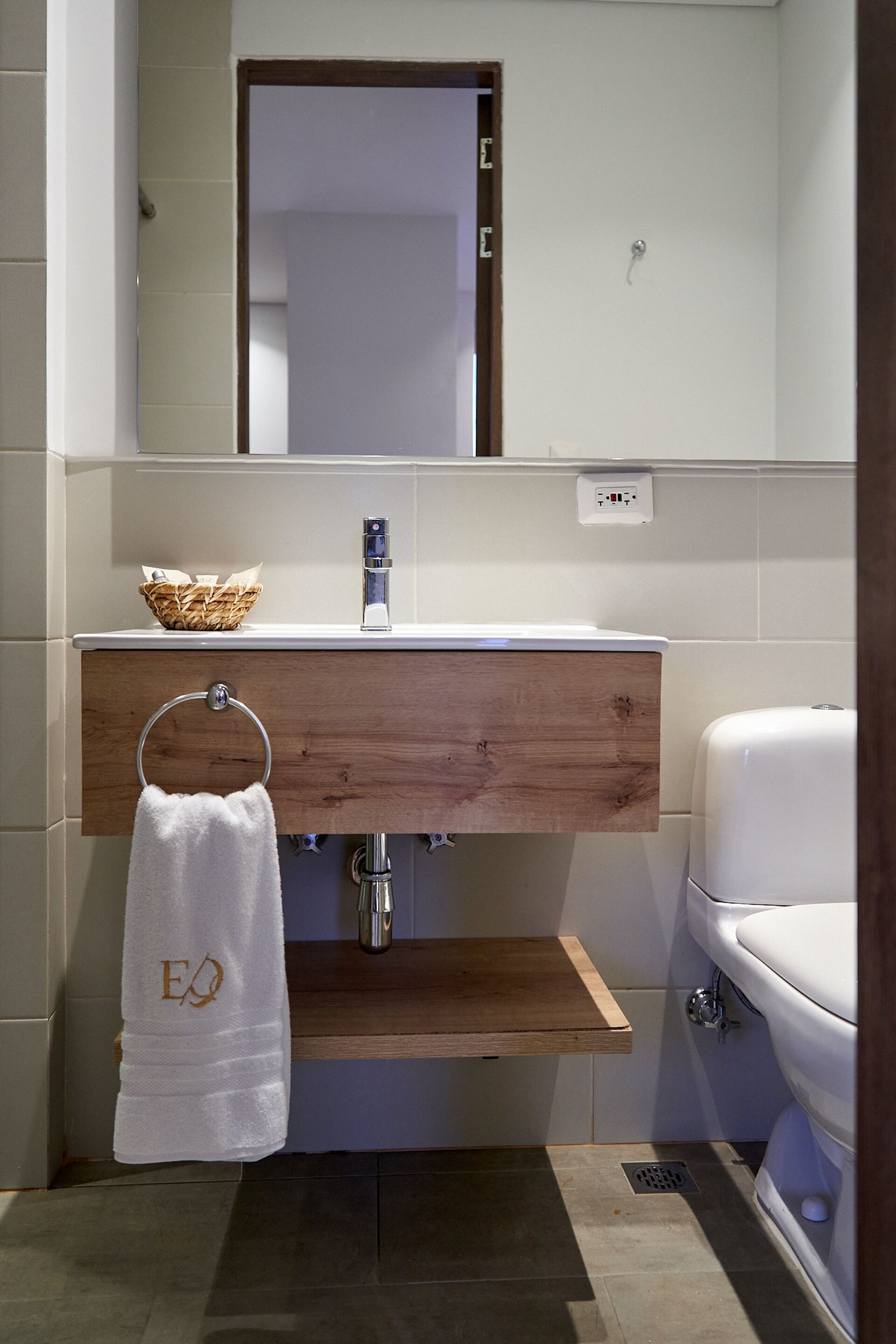 Un baño con tocador de madera, lavamanos blanco, toallero con toalla y un inodoro blanco.