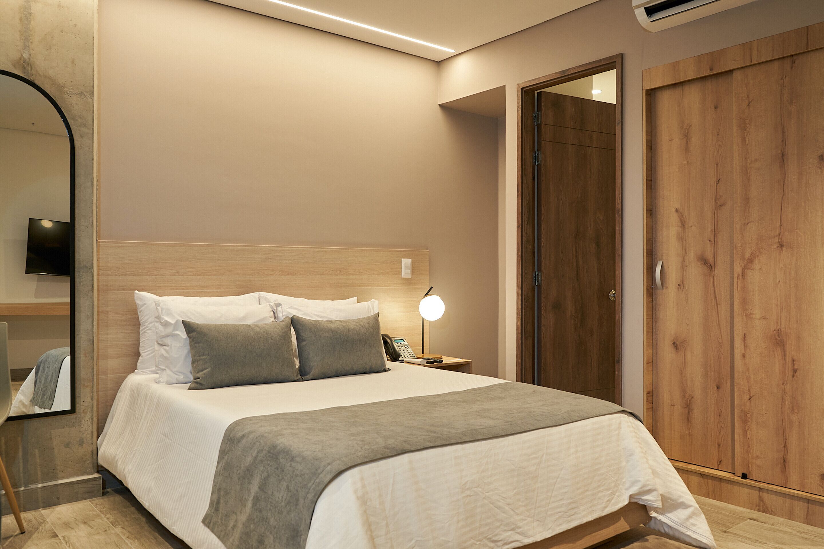 A modern bedroom with a large bed, bedside lamp, and a wooden wardrobe.