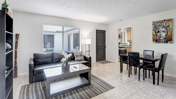 A modern living room with a black leather sofa, a glass coffee table, and a dining area with a black table and chairs. - Beautiful 1bd, prime location, free parking, bbq, pets (Delray Beach)