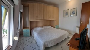A bedroom with a bed, a wardrobe, a desk with a computer, and a window.