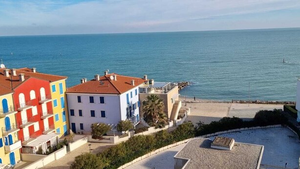 A coastal building with colorful facades, a beach in the background, and a clear view of the sea.