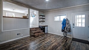 Ein geräumiger Raum mit Holzboden, einer eingebauten Treppe, einer Küchenzeile mit Spüle und Schränken sowie einer Tür mit Fenster.