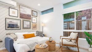 Un dormitorio con cama, mesitas de noche, una silla, una ventana y decoración en la pared.