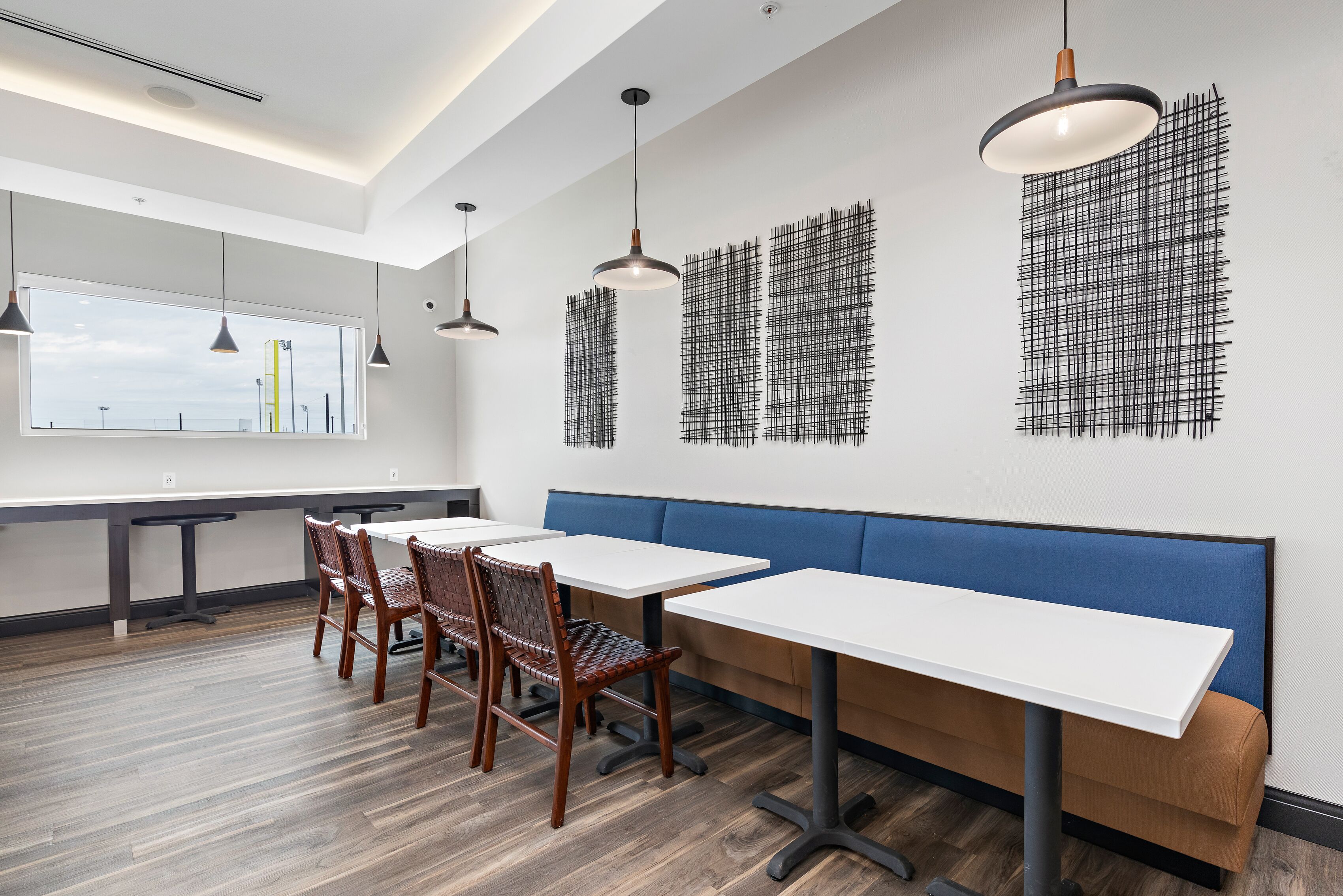 A modern office space with white tables, blue seating, and hanging pendant lights.