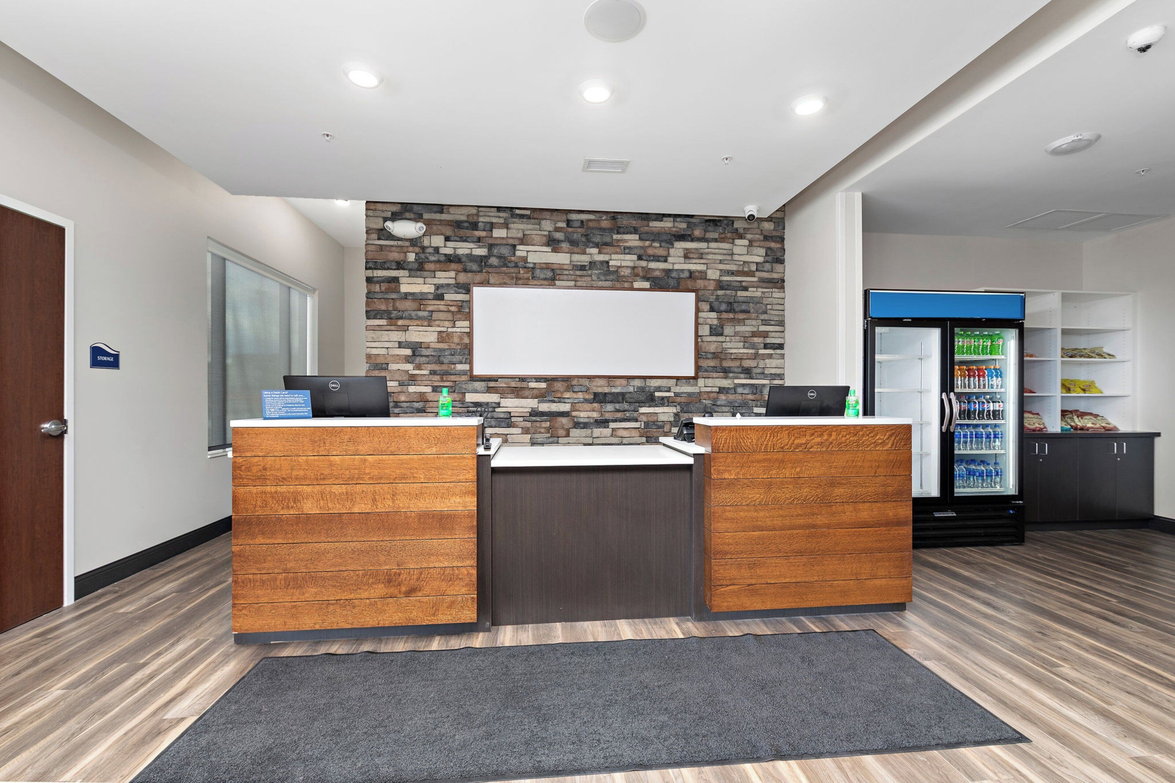 A reception area with a stone wall, two wooden counters, a whiteboard, and a refrigerator stocked with beverages.
