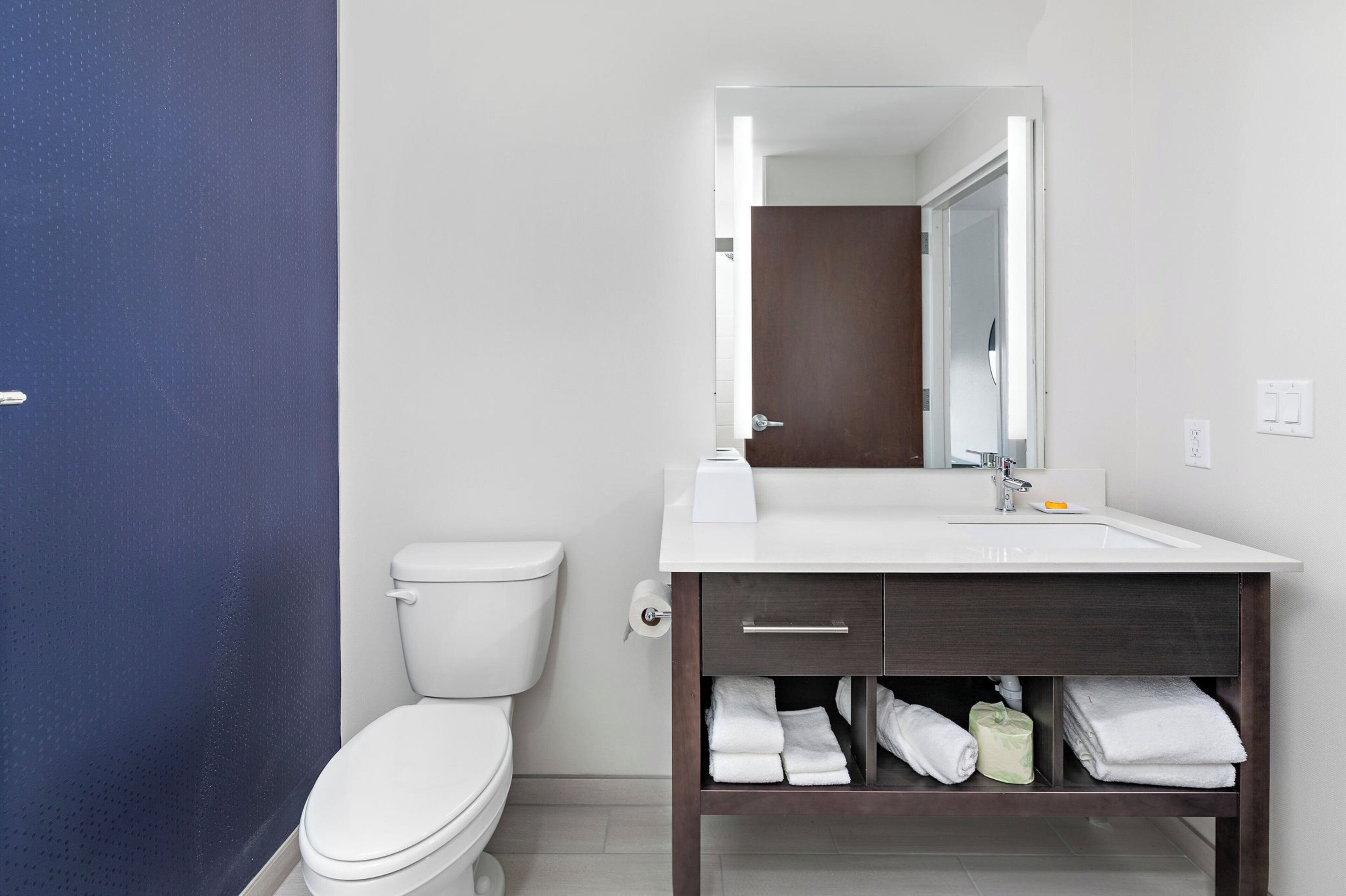 A modern bathroom with a toilet, a sink with a mirror, and a towel rack with folded towels.