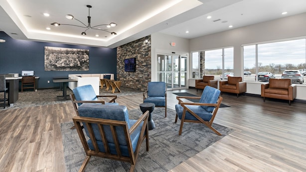 A modern lobby with seating areas, a stone accent wall, and large windows offering a view of parked cars and a cloudy sky. - Holiday Inn Express Kansas City North – Parkville by IHG (Parkville)