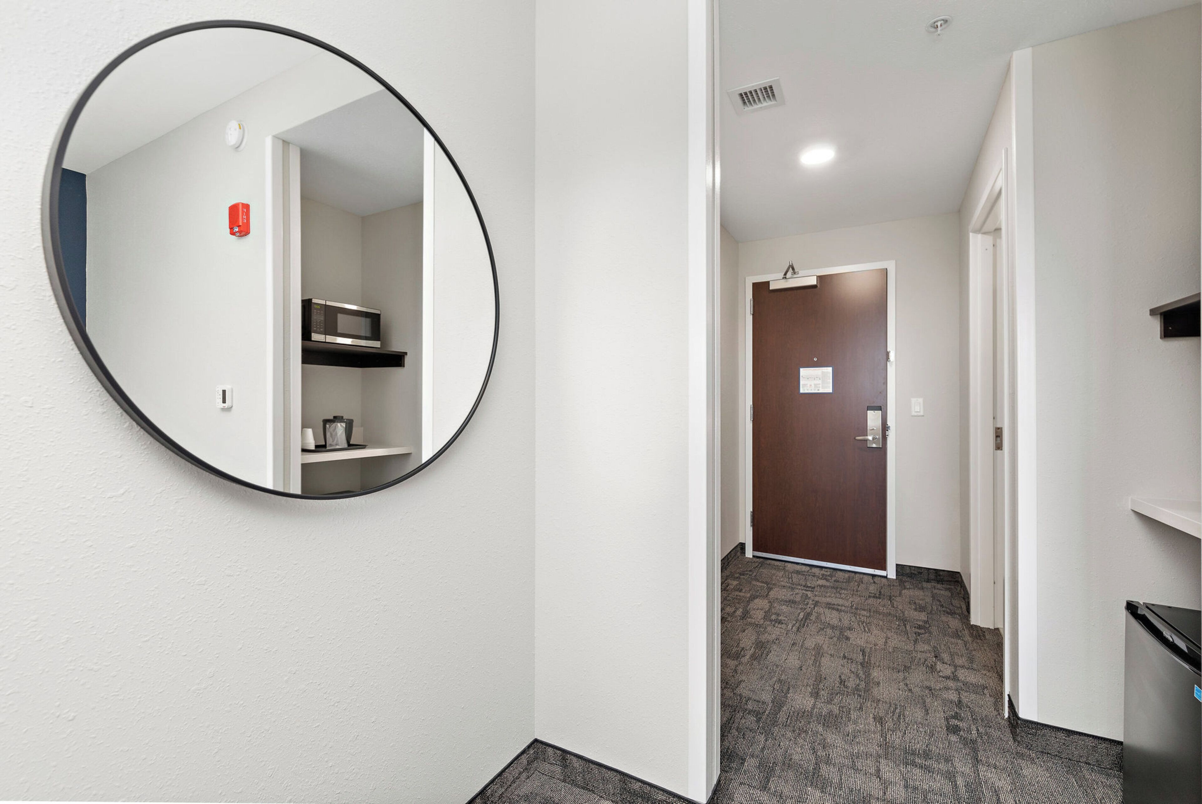 A hallway with a round mirror, a microwave on a shelf, and a door with a sign.