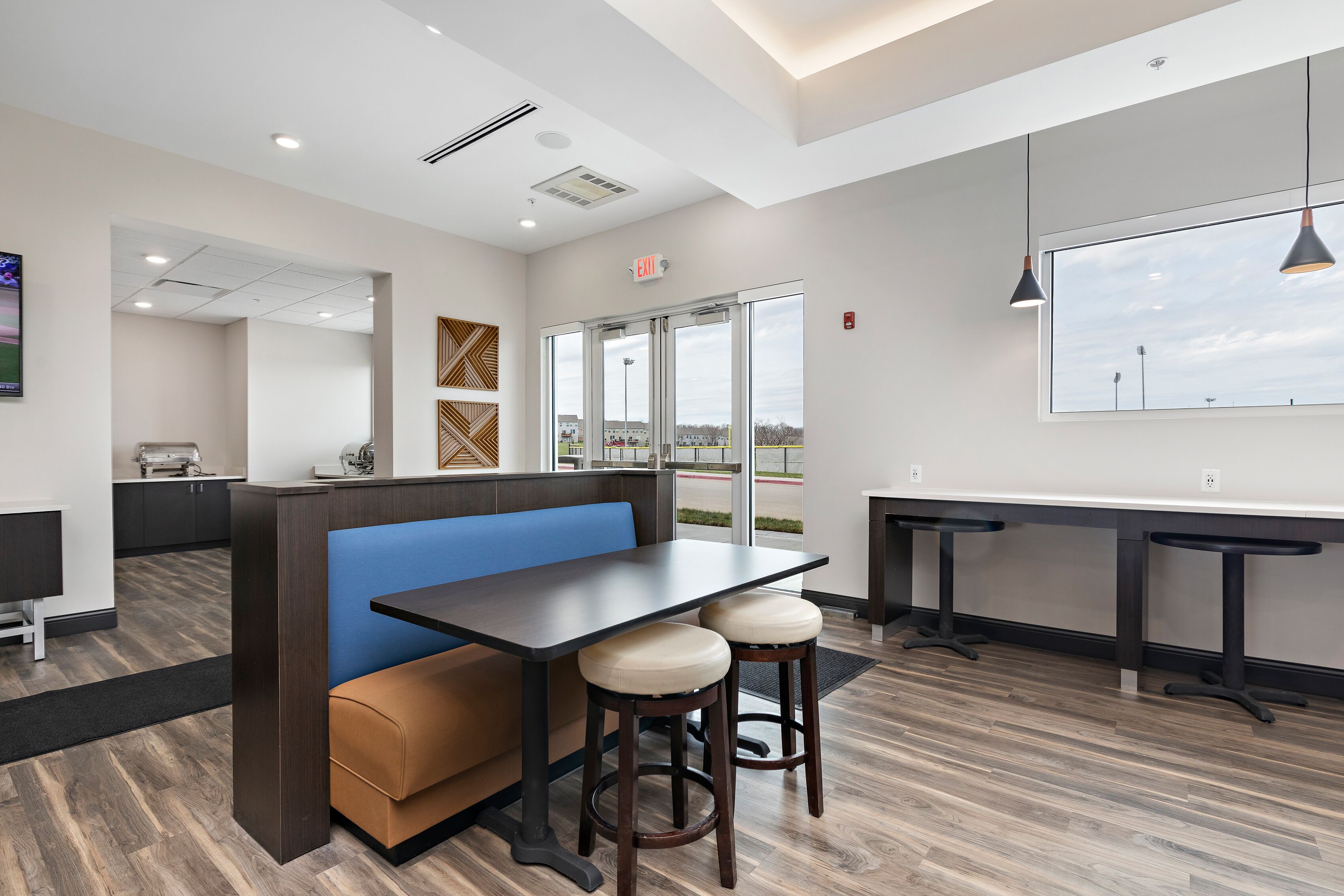 L’intérieur d’un restaurant moderne présente un coin salon avec des banquettes, une longue table avec des tabourets et une vue dégagée grâce à de grandes fenêtres.