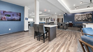 A modern hotel lobby with a wooden floor, a large TV on the wall, and a seating area with tables and chairs. - Holiday Inn Express Kansas City North – Parkville by IHG (Parkville)