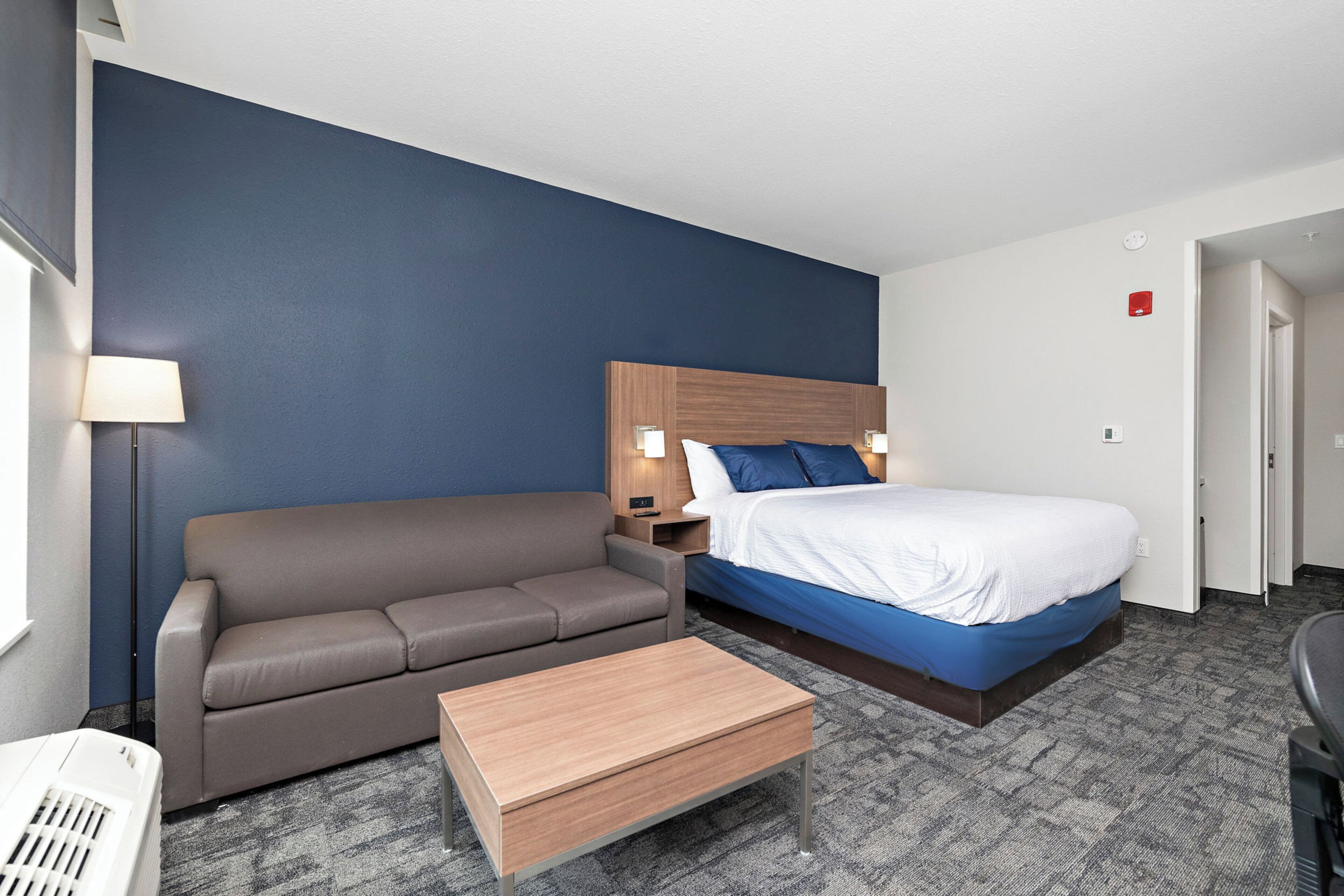Quarto de hotel com cama, sofá, mesa de cabeceira e uma pequena mesa.