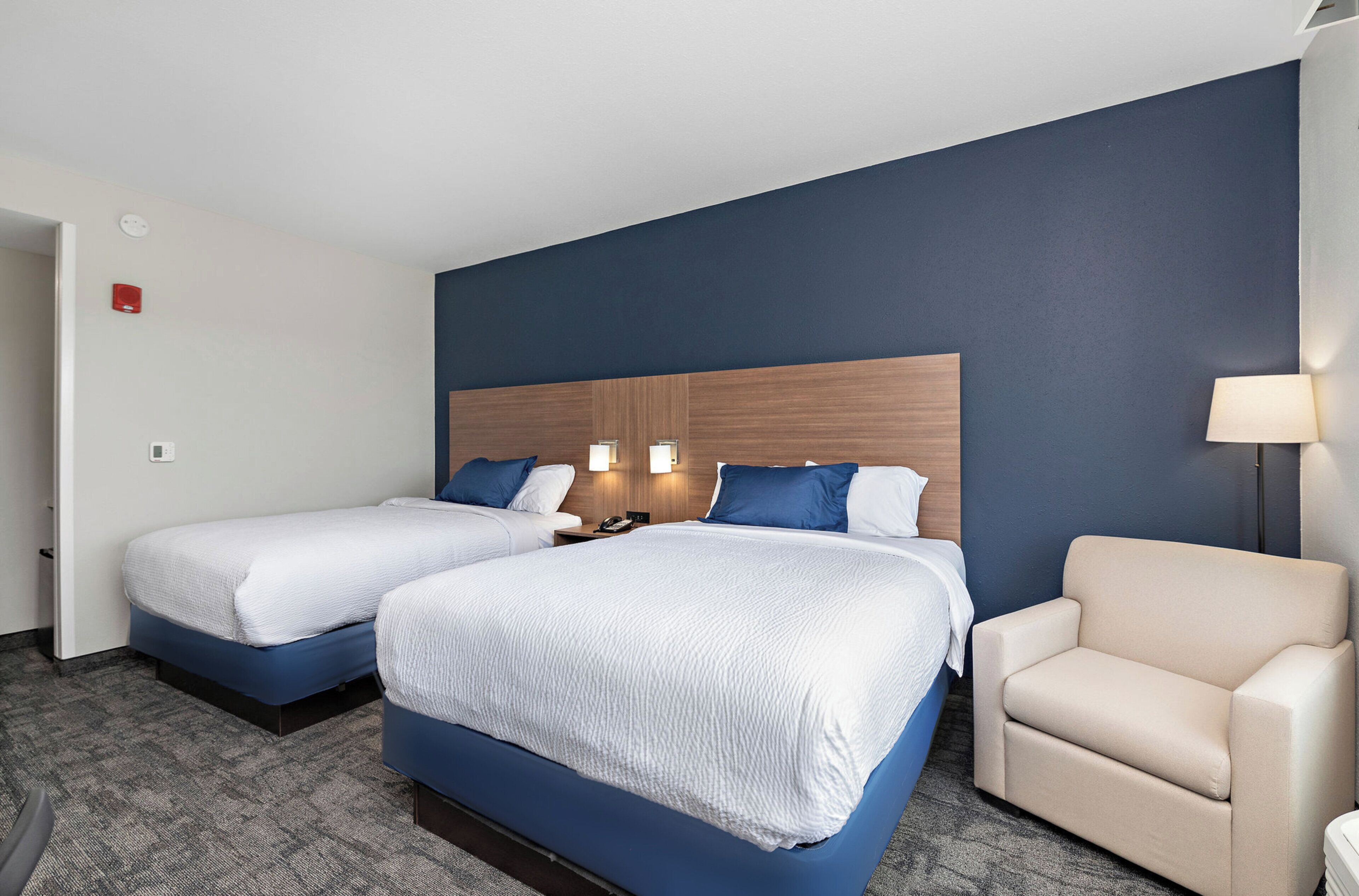Habitación de hotel con dos camas, una silla y una lámpara.