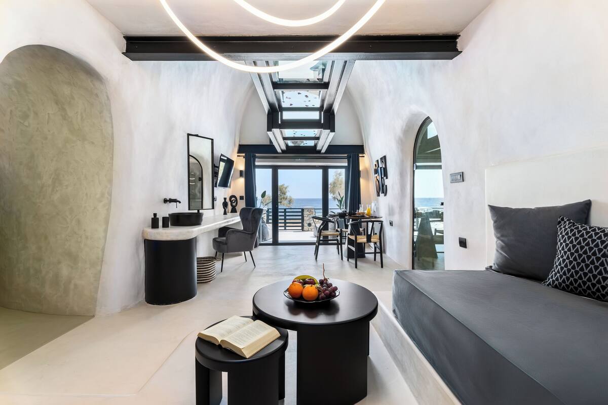 A modern interior with a sofa, a round table with fruit, and a view of the outdoors.
