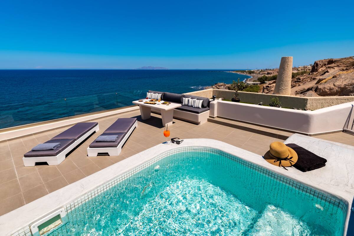 A poolside area with lounge chairs, a small table with drinks, and a view of the sea.