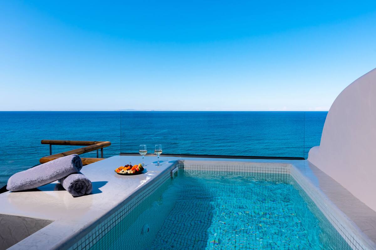 A poolside area with a view of the sea, a towel, a fruit plate, and two glasses.