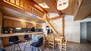 A spacious kitchen with a wooden staircase, a dining area with a stone island, and black chairs. - LA RECHASSE - Proche des pistes (Termignon)