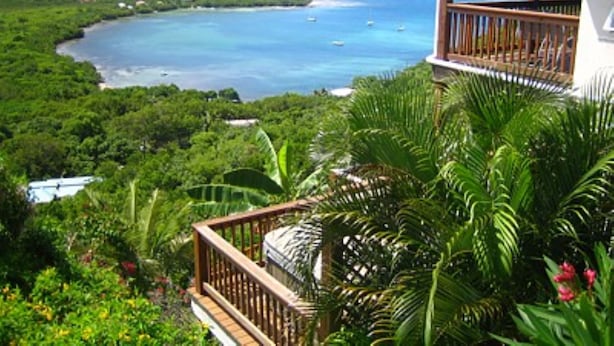 A tropical resort with a balcony overlooking a bay with boats, lush greenery, and a mountain in the background. - San Costanzo 2 br/ba Delightful breezes, Caribbean views, hot tub and generator! (St.John)