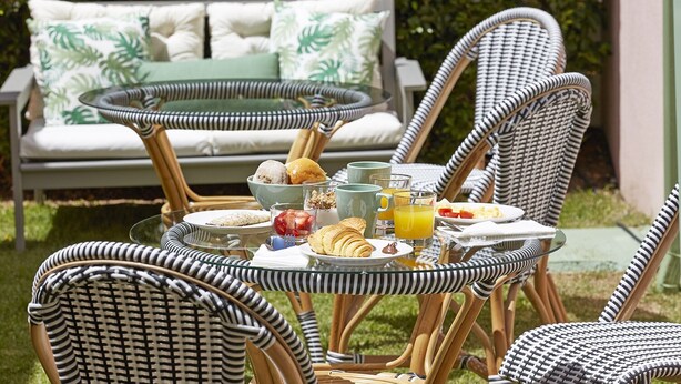 A breakfast setup with wicker chairs, a glass table, and a sofa with patterned cushions in a garden setting. - Sintra Green Chalet - Bed & Breakfast (Sintra)