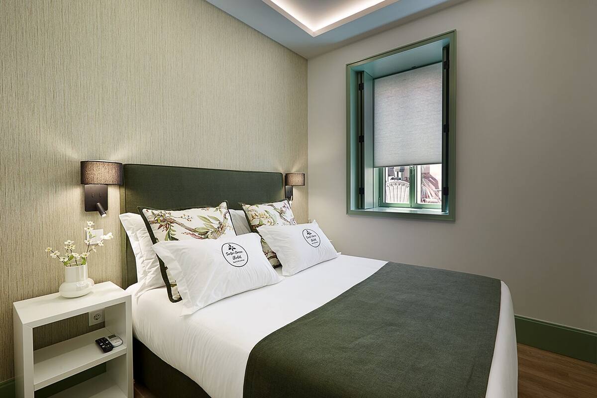 A neatly arranged bedroom with a bed, pillows, a bedside table, and a window with a view.