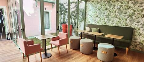 Une chambre moderne avec une grande fenêtre, un canapé vert, une petite table et deux poufs.