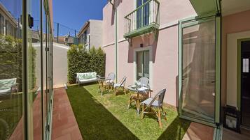 Une terrasse avec une petite table et des chaises, un canapé et une haie.
