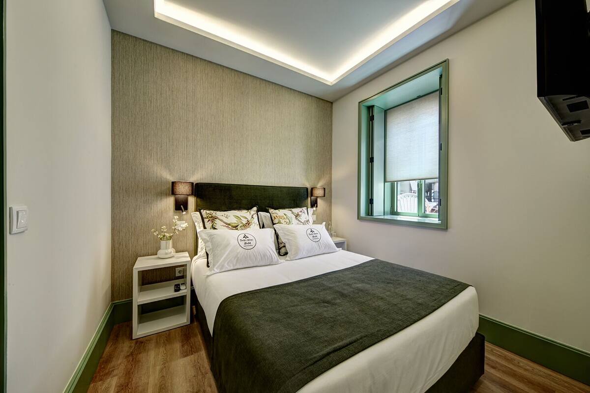 A modern bedroom with a bed, bedside tables, a nightstand, a window with a view, and a ceiling light fixture.