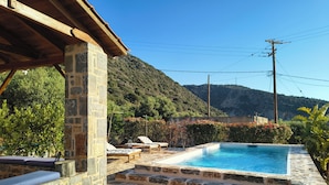 Una piscina de piedra con sillones de descanso, un muro de piedra y vistas a la montaña.