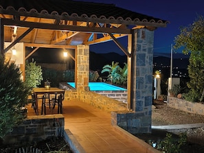 An outdoor patio area with a pool, stone walls, and a pergola structure. - Olive grove house of Polymnia (Επάνω Σίσι)